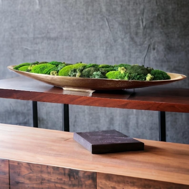 May include: A long, gold-colored, oval-shaped planter filled with a variety of green moss. The planter is sitting on a wooden table.
