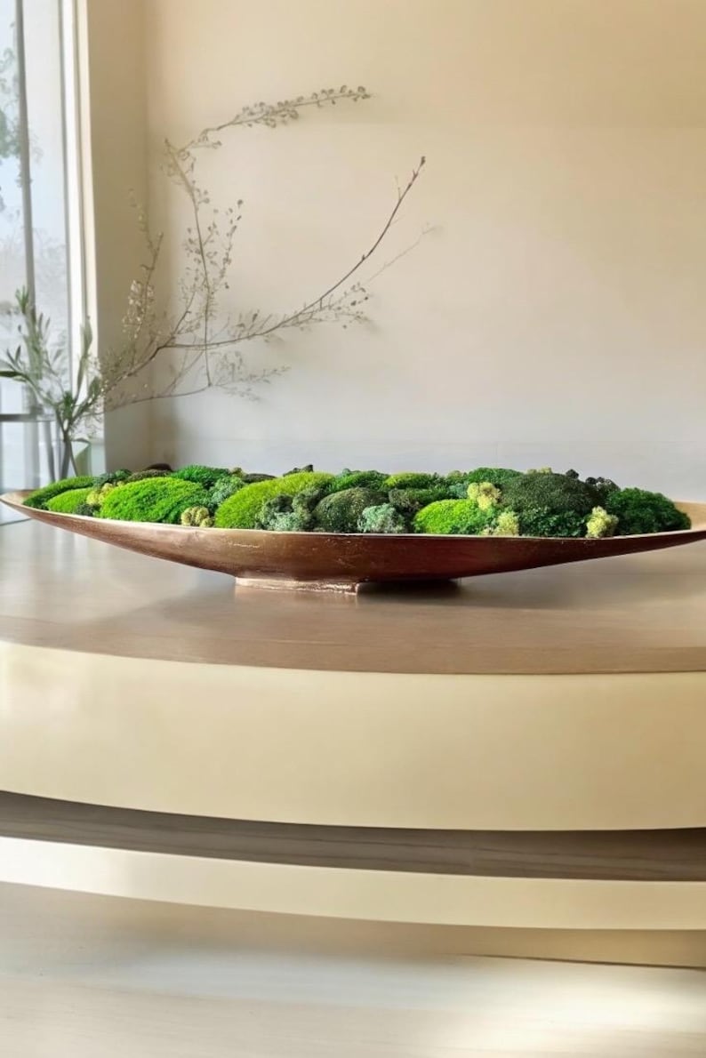 May include: A long, shallow, oval-shaped bowl with a metallic bronze finish filled with a dense arrangement of preserved green moss in various shades, including bright lime, deep forest green, and pale yellow-green textures.