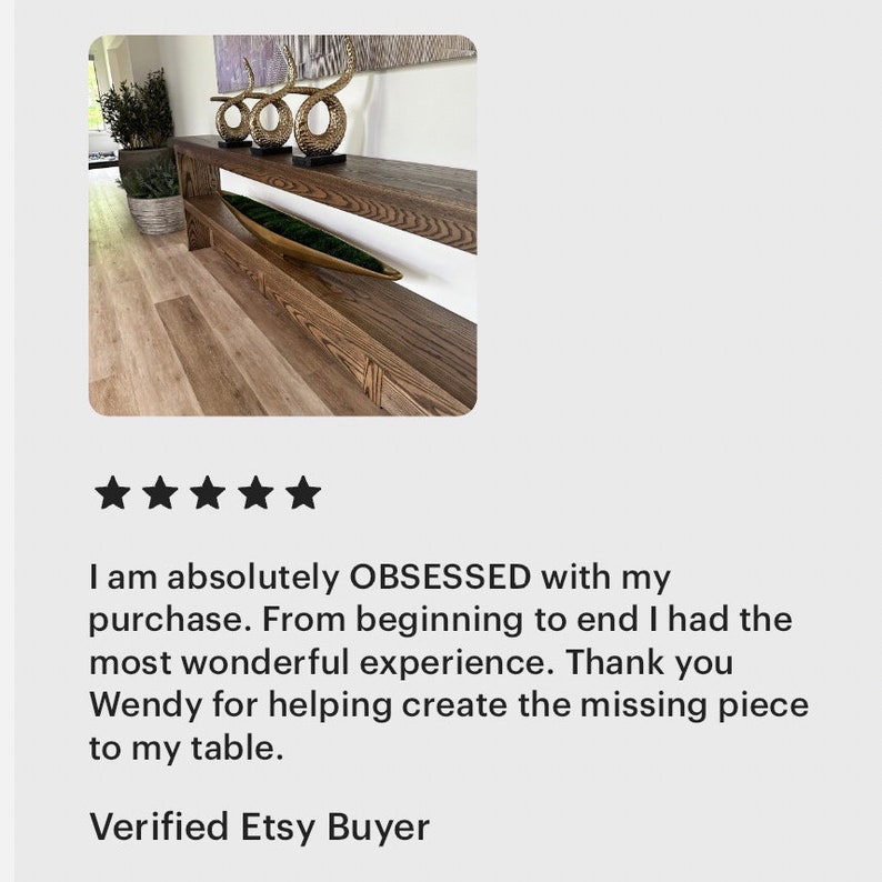 May include: A long, narrow wooden console table with a dark brown wood grain finish, featuring a lower shelf and a flat top surface. Three gold-colored, curved, horn-shaped decorative objects are placed on the top, and a long, shallow, boat-shaped bowl filled with green moss sits on the lower shelf.