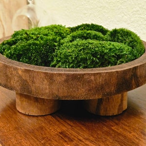 May include: A round, dark brown wooden bowl with a thick rim and three short, cylindrical wooden legs. The interior of the bowl is filled with a dense, vibrant green preserved moss that rises slightly above the top edge of the wooden container.