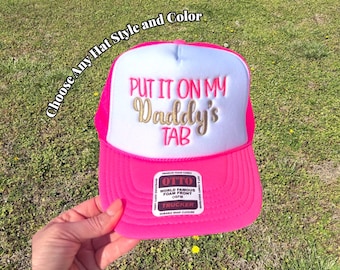 May include: A bright neon pink trucker hat with a white foam front panel. The text "PUT IT ON MY Daddy's TAB" is embroidered in pink and gold script. A rectangular sticker on the brim reads "OTTO WORLD FAMOUS FOAM FRONT OSFM TRUCKER".