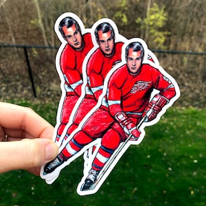 May include: Three hockey player stickers featuring a red, white, and blue hockey uniform with a stick and a puck. The players are in various poses, with one player holding a stick and puck, another player skating, and the third player in a defensive stance.