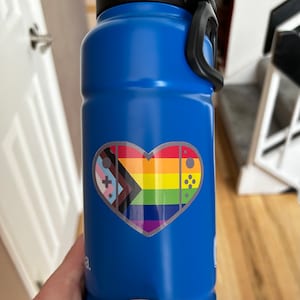 May include: A blue water bottle with a heart-shaped sticker. The sticker features a rainbow pride flag and a video game controller design.