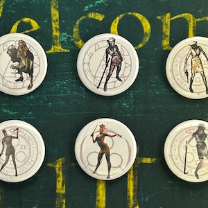 May include: Six white round pinback buttons with black and white images of characters from the Silent Hill video game series. The characters are all wearing nurse outfits and holding weapons. The buttons are arranged in a circle on a green surface.