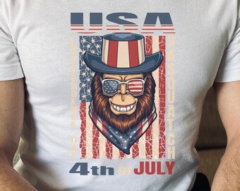 Puede incluir: Camiseta blanca con un gráfico de un mono de dibujos animados que lleva un sombrero de copa rojo, blanco y azul y gafas de sol. El mono está delante de una bandera estadounidense con el texto "USA Independence Day 4th of July" impreso en la camiseta.
