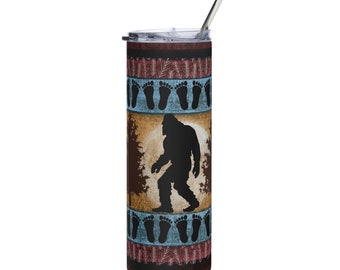 May include: A stainless steel tumbler with a brown, blue, and red design featuring a silhouette of Bigfoot walking through a forest. The design also includes footprints.
