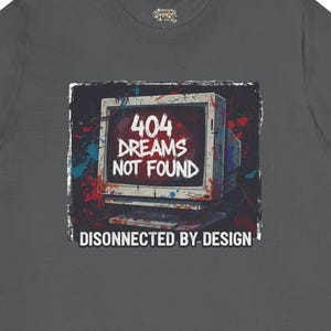 May include: Dark grey t-shirt with a retro computer graphic. The design includes the text "404 DREAMS NOT FOUND" and "DISCONNECTED BY DESIGN." The graphic has red, blue, and white accents, giving a vintage, distressed look. The shirt is made of a soft material.