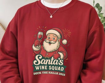 May include: A burgundy sweatshirt features a graphic of Santa Claus holding a glass of wine. The text reads "Santa's Wine Squad Deck the Halls 2025". The design includes a red Santa hat and a white beard.