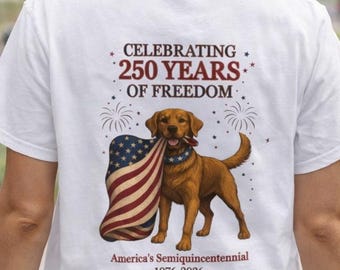 May include: White t-shirt featuring a brown Labrador Retriever holding an American flag in its mouth. The shirt has the text "Celebrating 250 Years of Freedom" and "America's Semiquincentennial 1976-2026".
