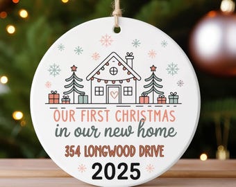 May include: A round, white Christmas ornament with a house graphic, Christmas trees, and snowflakes. Text reads "OUR FIRST CHRISTMAS in our new home 354 LONGWOOD DRIVE 2025". The ornament hangs from a natural twine string.