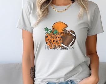 May include: A gray t-shirt with a graphic of a football helmet, a football, and a pumpkin with a leopard print design. The text "Tis the Season" is printed below the graphic.