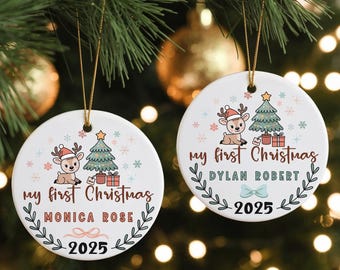 May include: Two white ceramic Christmas ornaments hanging from a green tree. Each ornament features a cartoon reindeer wearing a Santa hat, a Christmas tree, and the text "my first Christmas". One ornament says "Monica Rose 2025". The other says "Dylan Robert 2025".