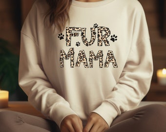 May include: A white sweatshirt with the text "FUR MAMA" in brown and black leopard print letters. The letters are outlined in black and have paw prints on either side of the text.