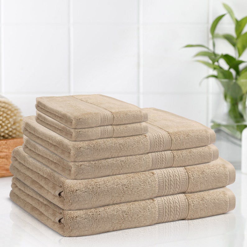 May include: A stack of six beige bath towels, folded and arranged in a pyramid shape. The towels are made of a soft, absorbent material and have a subtle texture.