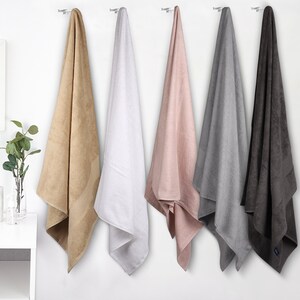 May include: Five bath towels hanging on hooks. The towels are in various colors, including beige, white, pink, gray, and dark gray.