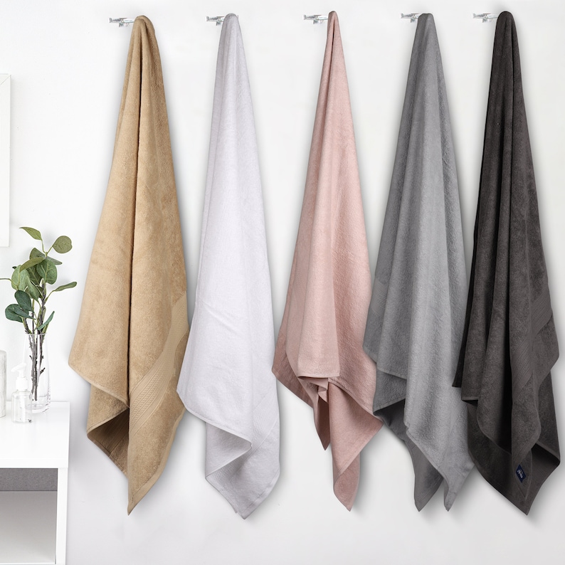 May include: Five bath towels hanging on hooks. The towels are in various colors, including beige, white, pink, gray, and dark gray.