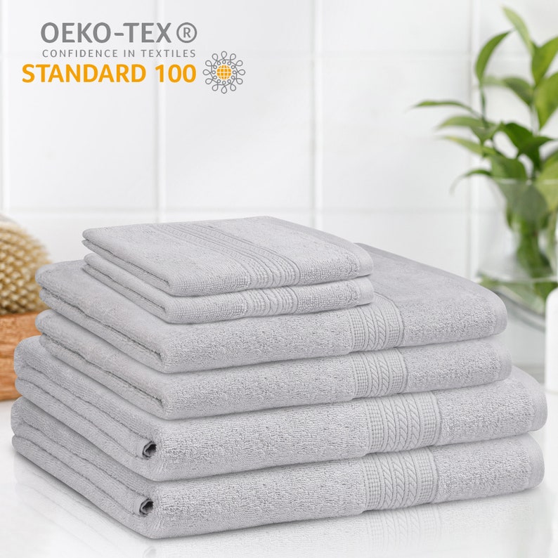 May include: A stack of six gray bath towels. The towels are made of soft, absorbent cotton and are certified Oeko-Tex Standard 100, meaning they are free of harmful chemicals.
