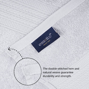 May include: Close-up of a white towel with a blue label that reads "essell&reg; SINCE 1997". The towel has a double-stitched hem and a natural weave, which are highlighted in the image.