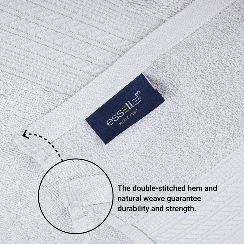 May include: Close-up of a white towel with a blue label that reads "essell&reg; SINCE 1997". The towel has a double-stitched hem and a natural weave, which are highlighted in the image.