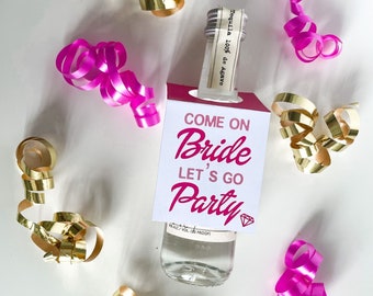 Puede incluir: Una botella blanca con una etiqueta rosa y blanca que dice "Come on Bride Let's Go Party". La botella está rodeada de cinta rosa y dorada.