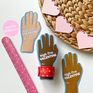 May include: Three printable Valentine's Day cards featuring a hand with the text "high five VALENTINE" and a space for a name. The cards are blue and brown with a red bracelet on one of the hands.