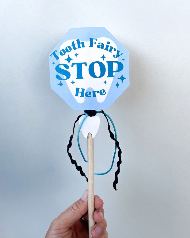 May include: A blue and white tooth fairy stop sign with the text "Tooth Fairy Stop Here" and a white tooth cutout attached to a wooden stick with blue and black string.