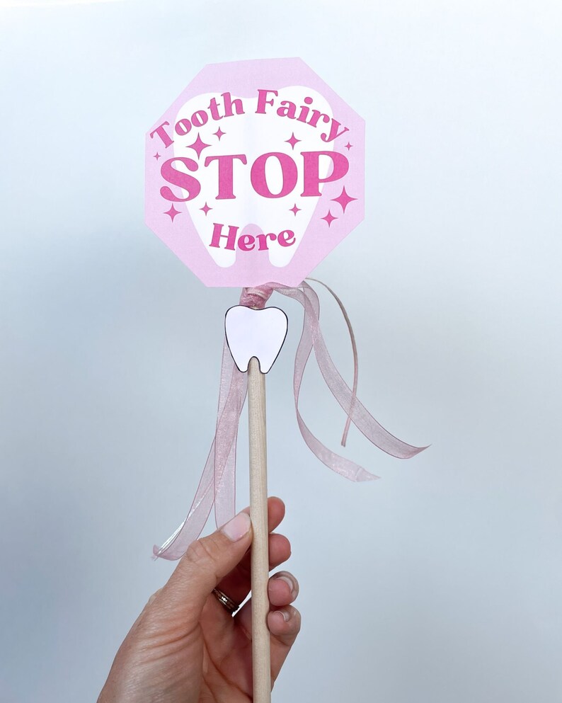 May include: Pink tooth fairy stop sign with the words "Tooth Fairy Stop Here" and a white tooth graphic. The sign is attached to a wooden stick with a pink ribbon.