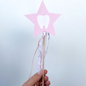May include: A pink star-shaped wand with a white tooth cutout and pink and white ribbons attached to the wooden stick.