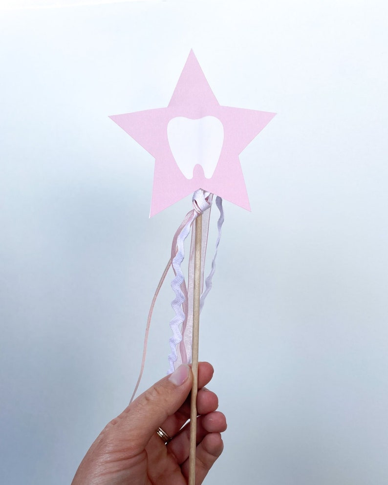 May include: A pink star-shaped wand with a white tooth cutout and pink and white ribbons attached to the wooden stick.