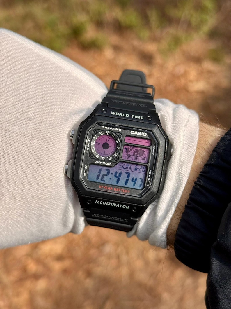 May include: A black Casio digital watch with a 10-year battery. The watch face displays the time, date, and day of the week. It also has a world time function, alarm, and stopwatch.