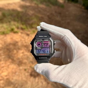 May include: Black Casio digital watch with a black strap. The watch face displays the time, date, and other features. The watch has a world time function and an illuminator.