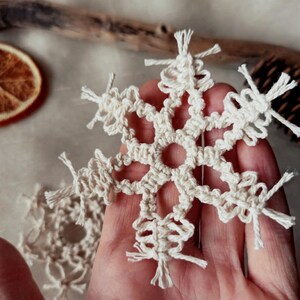 May include: A white crocheted snowflake ornament with a delicate design and fringed edges.