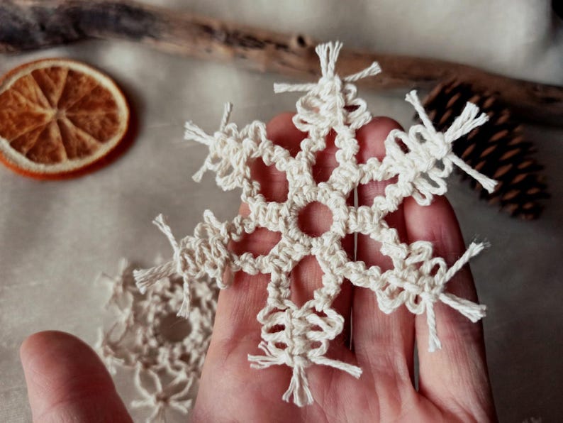May include: A white crocheted snowflake ornament with a delicate design and fringed edges.