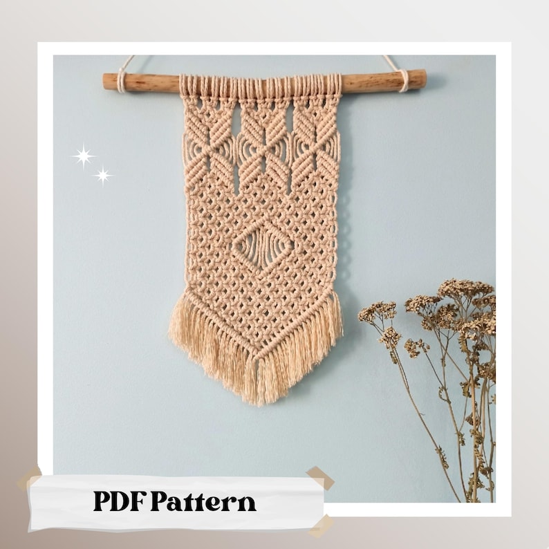 May include: A beige macrame wall hanging with a geometric pattern and fringe. The hanging is attached to a wooden dowel rod and is displayed against a light blue wall.
