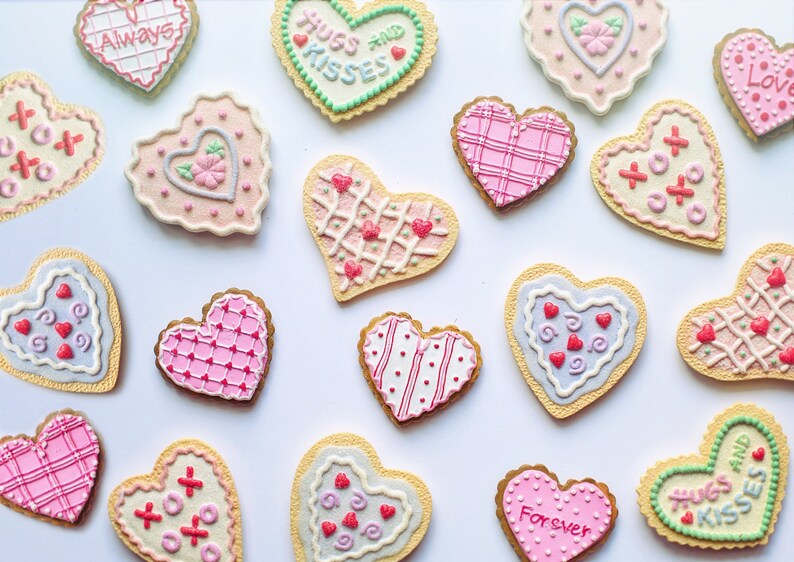 Pu&ograve; includere: Assortimento di biscotti a forma di cuore decorati con vari motivi e messaggi, tra cui "Always", "Hugs and Kisses", "Forever" e "Love".
