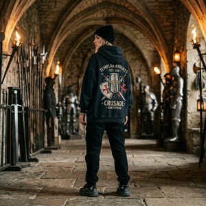 May include: A black hooded sweatshirt featuring a graphic on the back with the text "TEMPLAR KNIGHTS EST. 1119 CRUSADE FORTITUDE" surrounding an illustration of a shield and two crossed swords with red cross accents, paired with black trousers.