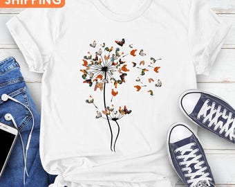 May include: White t-shirt with a dandelion design made of chickens. The dandelion is made of chickens with butterfly wings. The t-shirt is on a white surface with a pair of blue jeans and a phone.