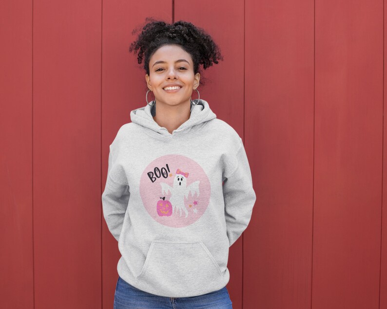 Puede incluir: Una sudadera gris con un gr&aacute;fico circular rosa que presenta un fantasma blanco con un lazo rosa, una calabaza y el texto "BOO!"