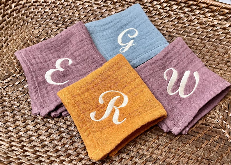 May include: Four fabric squares with embroidered letters. The squares are in shades of pink, blue, yellow, and orange. The letters are E, G, W, and R.