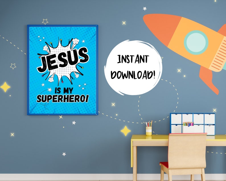 Op de afbeelding: Een blauw en wit printbaar wanddecoratiedesign met de tekst "JESUS IS MY SUPERHERO!" in een stripboek stijl. Het ontwerp is ingelijst en wordt weergegeven op een blauwe muur met een raket en sterren.