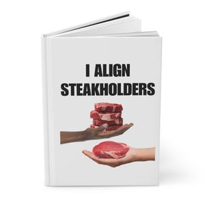 May include: A white notebook with the text "I Align Steakholders" in black. The image shows a stack of raw steaks on a hand, and a single steak on another hand.