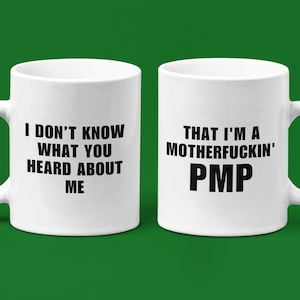 May include: A white ceramic mug with a black handle and the text "But First, Coffee" in a black, handwritten-style font. The mug is on a white surface.
