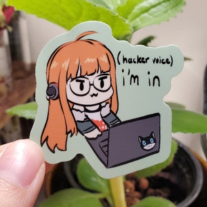 Peut inclure: Un autocollant représentant un personnage de dessin animé avec des cheveux orange, portant des lunettes et un casque, assis devant un ordinateur portable avec un visage de chat sur l'écran. Le texte sur l'autocollant est "(hacker voice) i'm in".