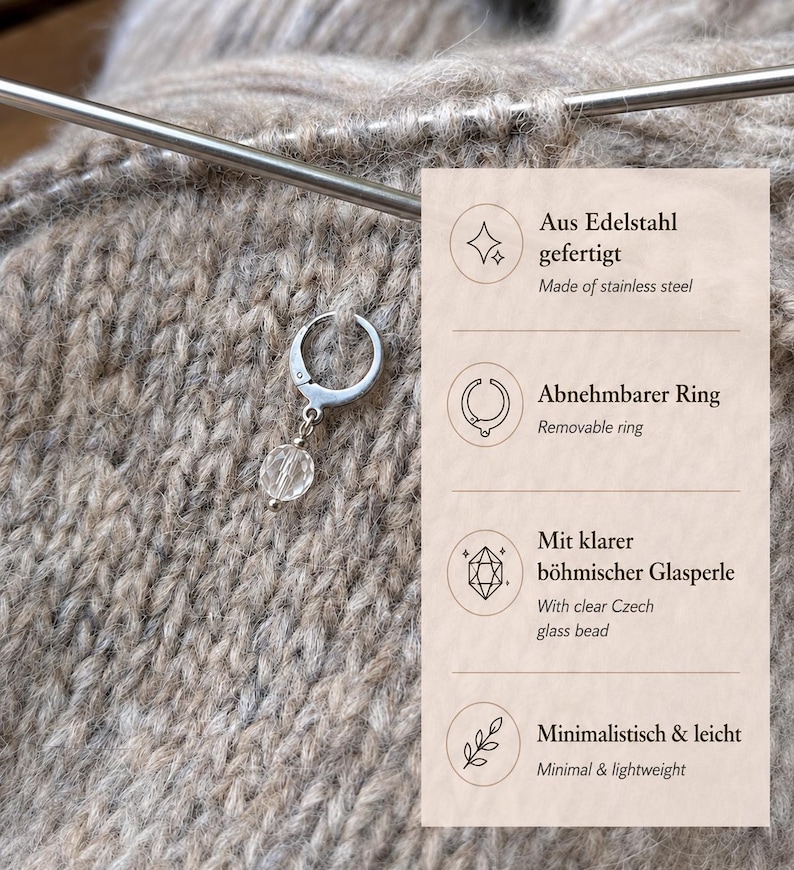 May include: A silver-toned stainless steel stitch marker ring featuring a clear faceted glass bead charm. The text on the right side lists features including Aus Edelstahl gefertigt, Abnehmbarer Ring, Mit klarer b&ouml;hmischer Glasperle, and Minimalistisch & leicht.