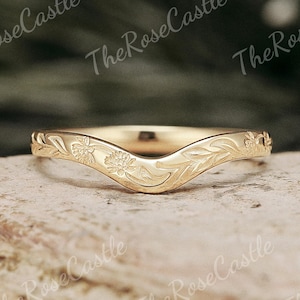 Op de afbeelding: Een goudkleurige, gebogen ring met bloemen- en bladgravures. De ring heeft een V-vormig ontwerp en is waarschijnlijk een trouwring of een decoratieve ring. De tekst The Rose Castle is zichtbaar.