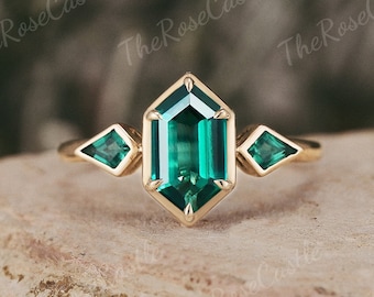 May include: A gold ring with a large emerald green octagon-shaped gemstone surrounded by two smaller emerald green triangular gemstones.