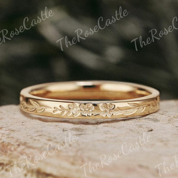 May include: A gold-toned metal ring featuring an engraved floral pattern with delicate leaves and small blossoms encircling the band. The surface of the ring has a polished finish, and the text TheRoseCastle is visible in the background.