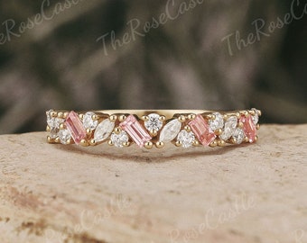 May include: A delicate gold band ring with a row of alternating pink and white gemstones. The ring features a mix of round and baguette-shaped stones.