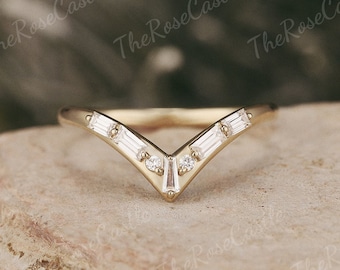 May include: A gold-colored V-shaped ring with small, rectangular and round gemstones. The ring is set on a light brown, textured surface. The Rose Castle is printed on the image.