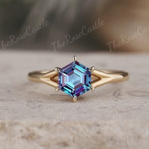 Könnte beinhalten: Ein goldener Ring mit einem hexagonalen Alexandrit-Edelstein. Der Edelstein ist tiefblau mit violetten und grünen Schimmern.